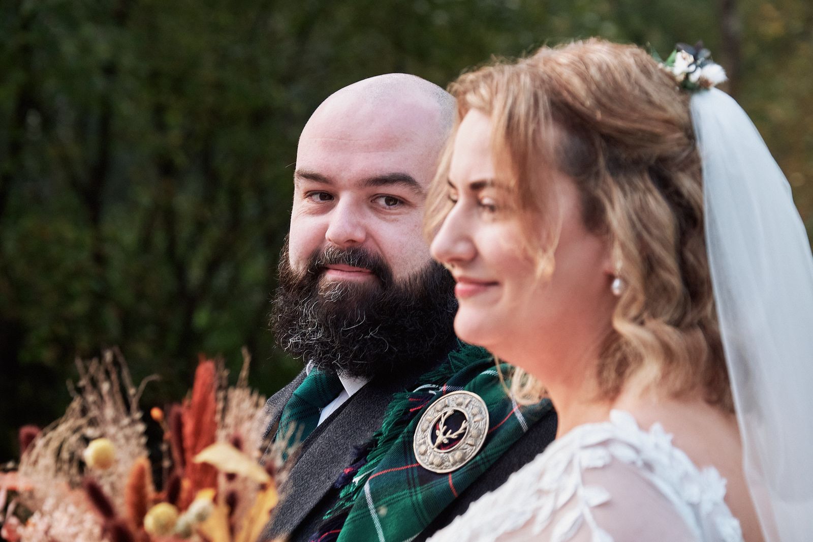 Close-up of the couple smiling side by side, with an autumn bouquet